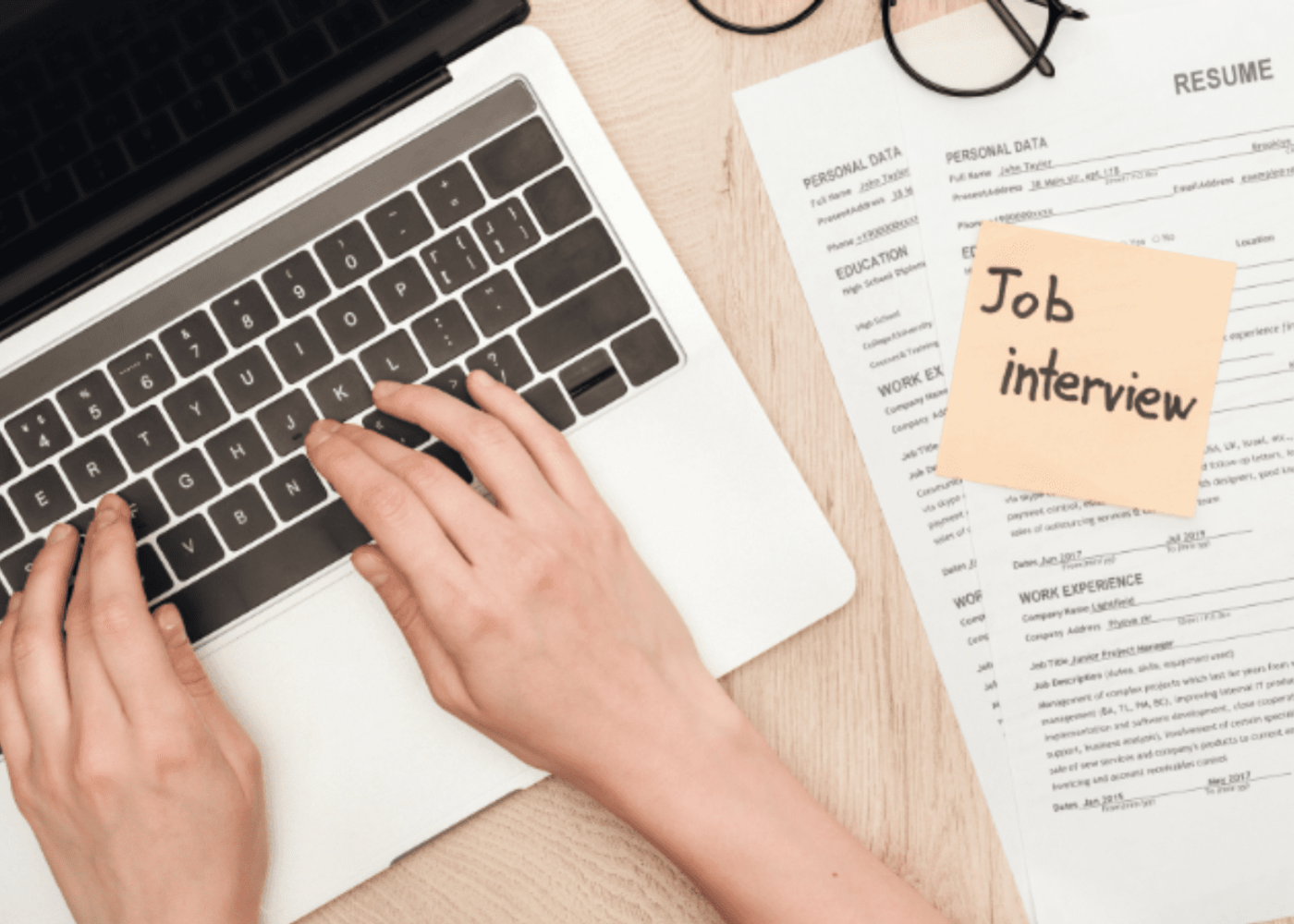 Person working on a laptop with their resume beside them and a note saying job interview.