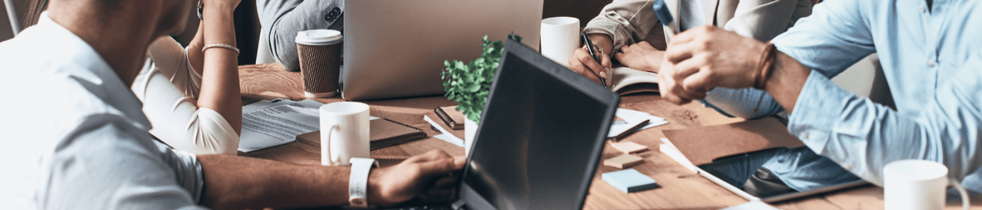 A table with business people meeting around it with their laptops, coffee cups and papers